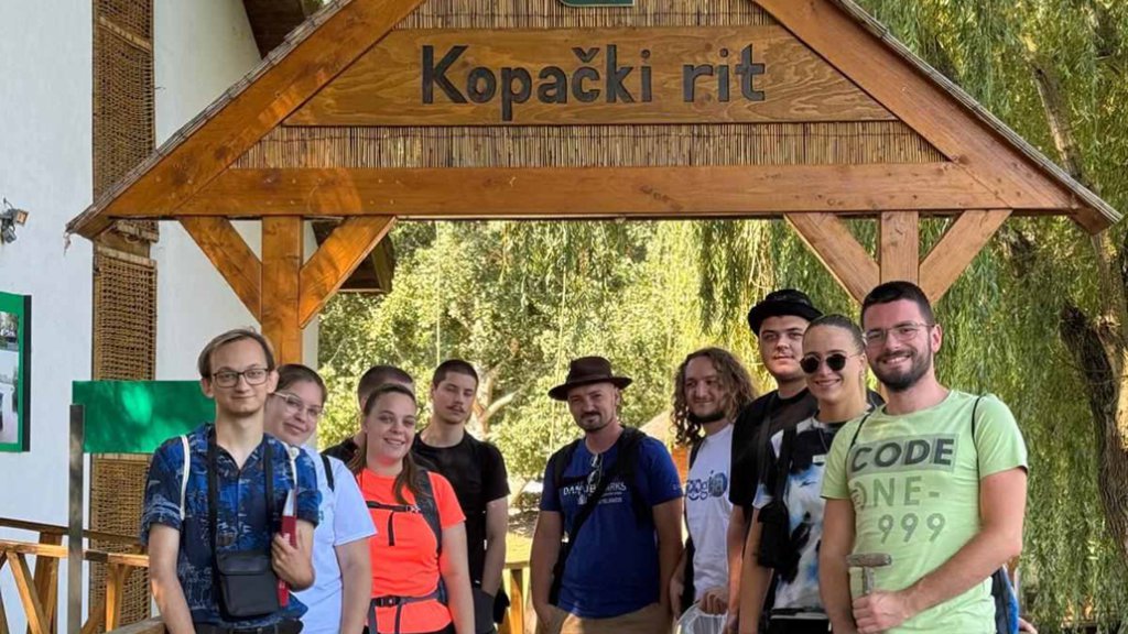 Several people gather outside under a wooden sign. 