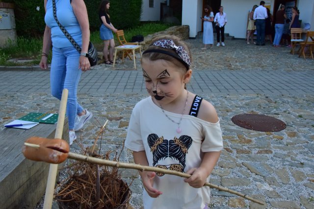 Young girl with face painted holds stick with sausage for a campfire