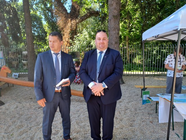 Two men stand outside under a tree. 
