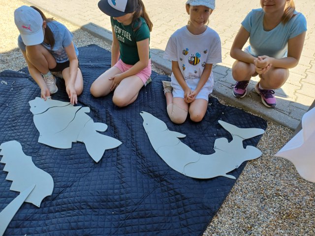 Four children sit on a black tarp with large fish cut-outs. 